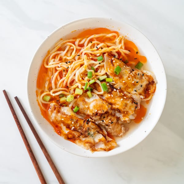 A bowl of ijji Noodle House's spicy ramen with dumplings, green onions, and sesame seeds.