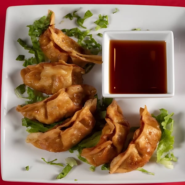 Golden-brown fried dumplings, garnished with lettuce, served with a side of dark dipping sauce.