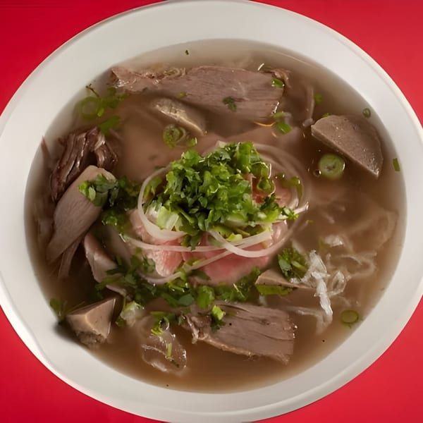 A bowl of ijji Noodle House pho with beef, noodles, and fresh herbs in broth.