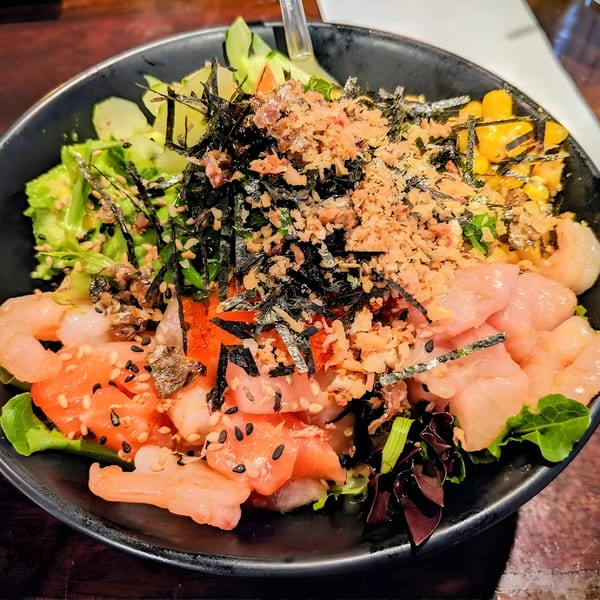 Close-up of a colorful poke bowl with salmon, shrimp, corn, seaweed, and various toppings.